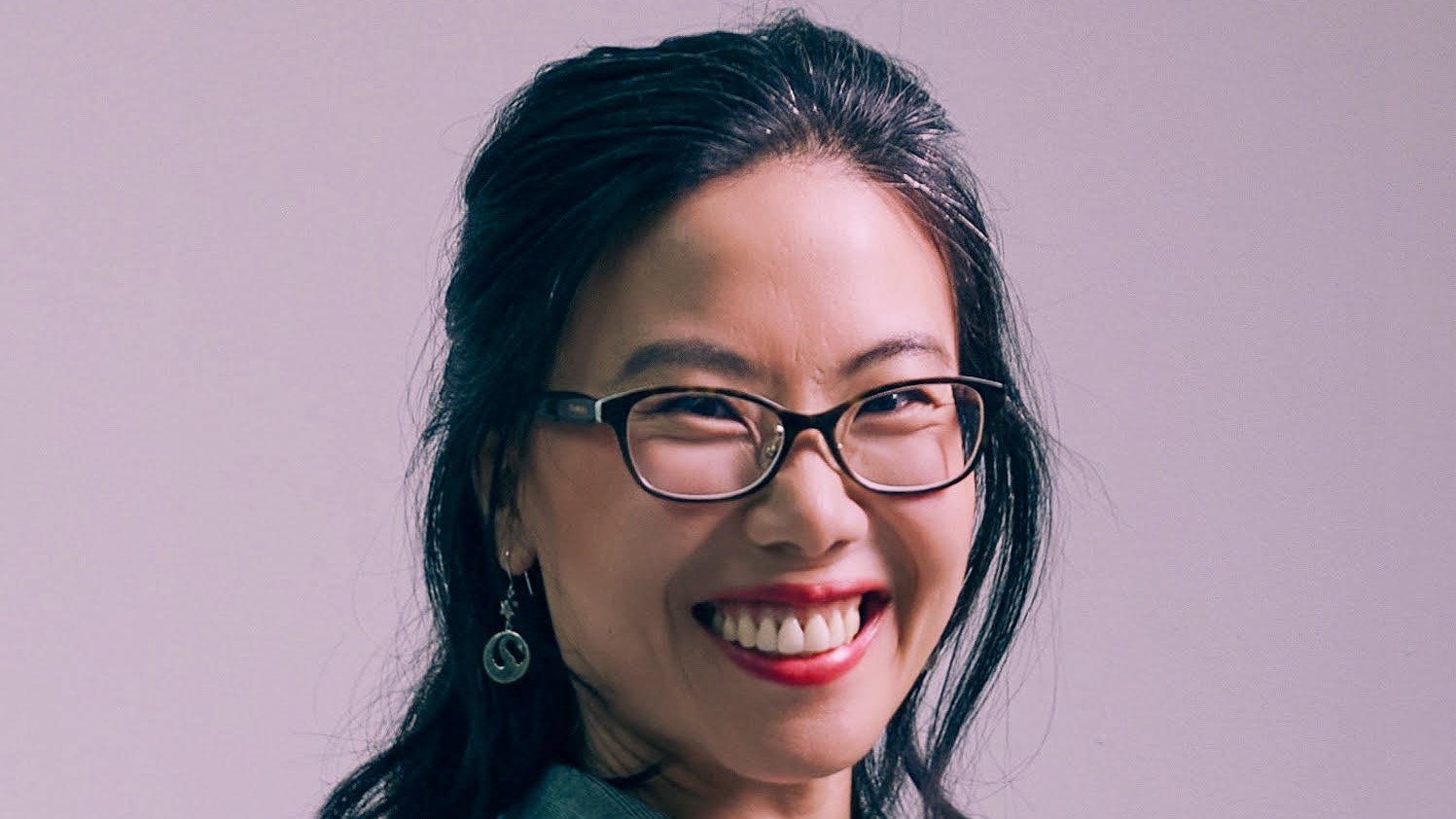 A young woman wearing glasses and red lipstick looks at the camera